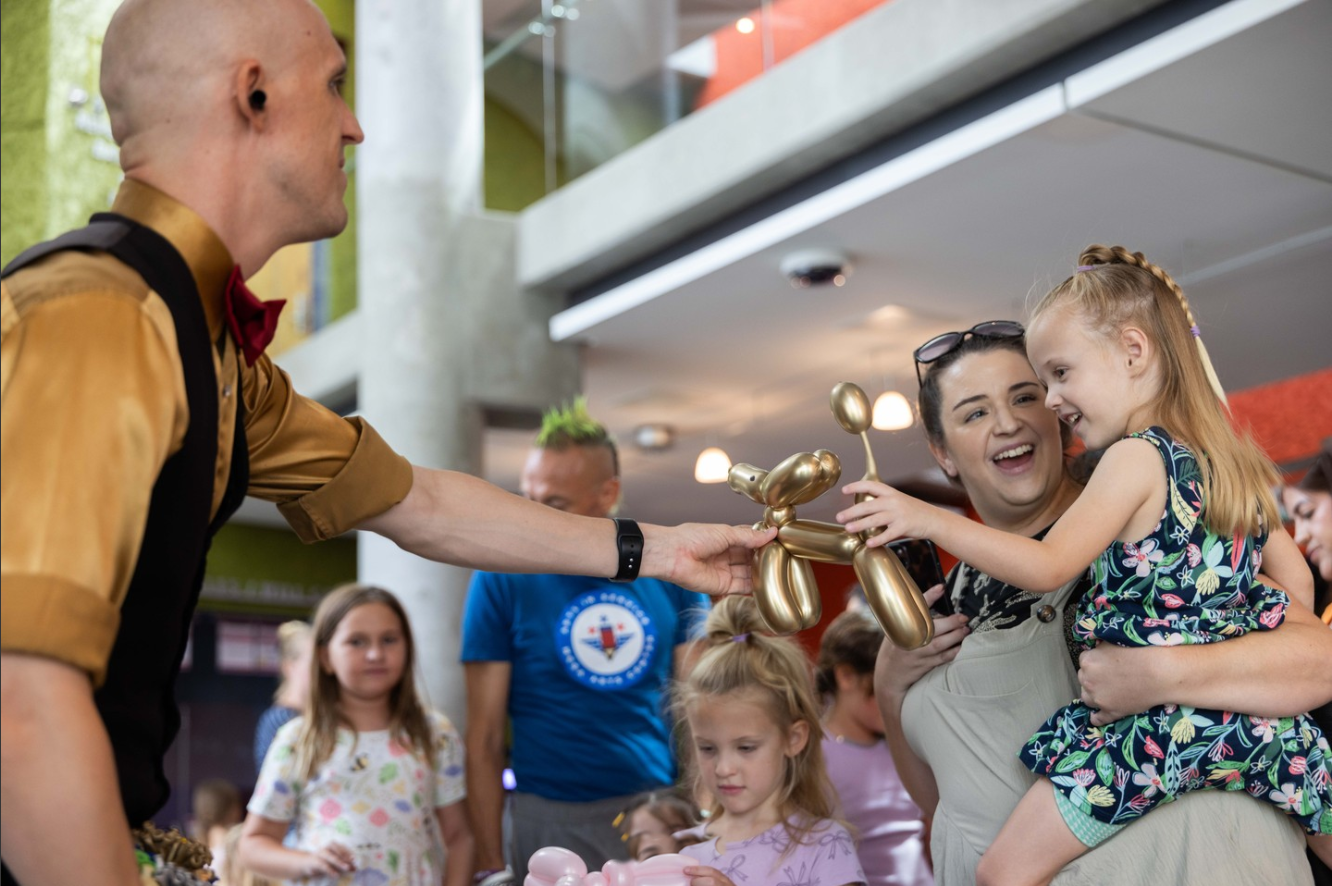 Dan handing a gold balloon dog to a smiling child at a family event