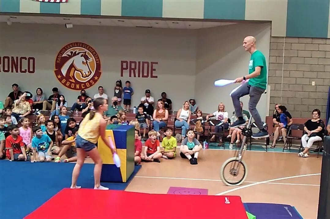 Dan juggling on a giraffe unicycle during an interactive school circus show