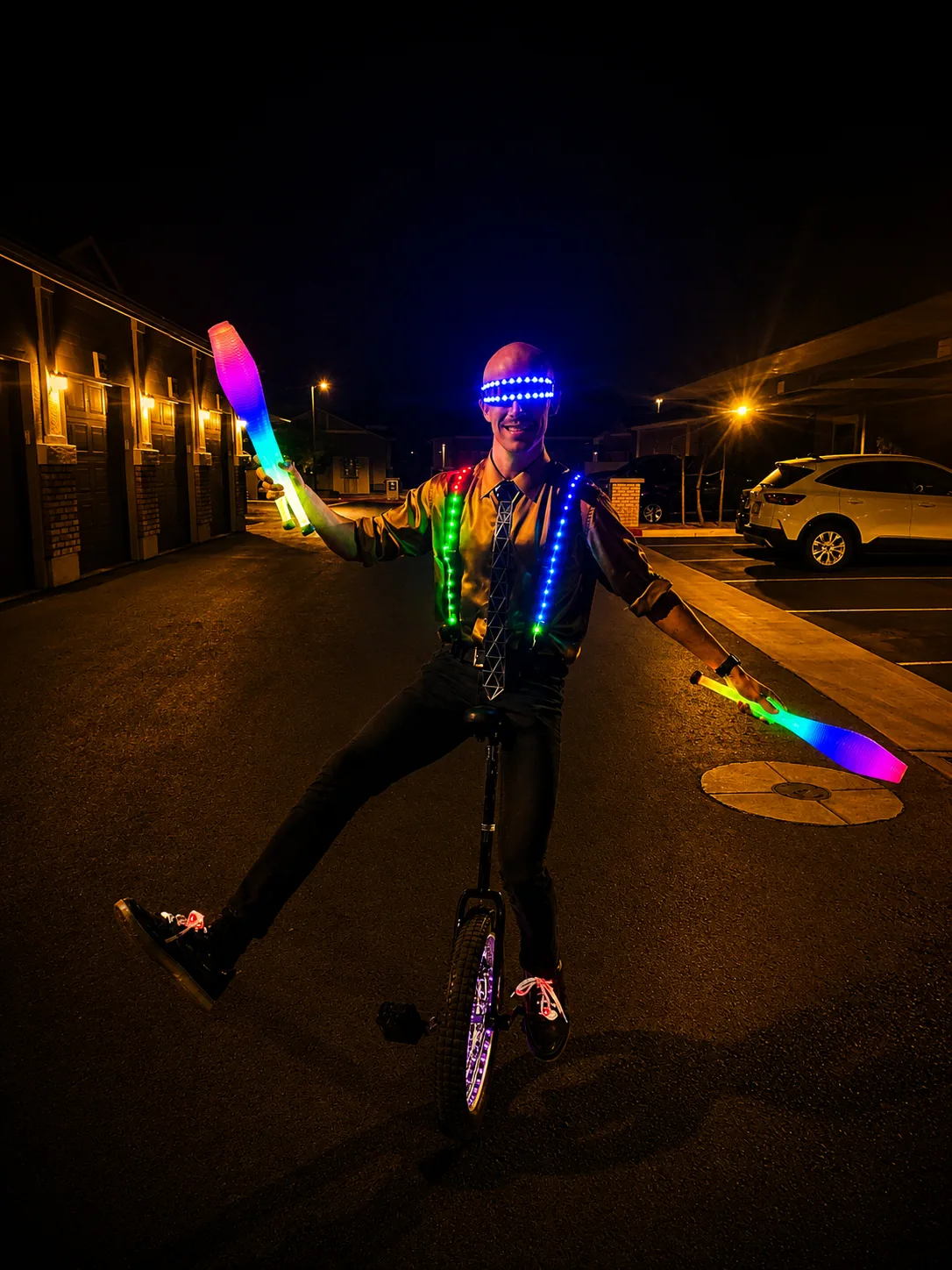 Dan balancing on an illuminated unicycle while presenting colorful LED juggling clubs
