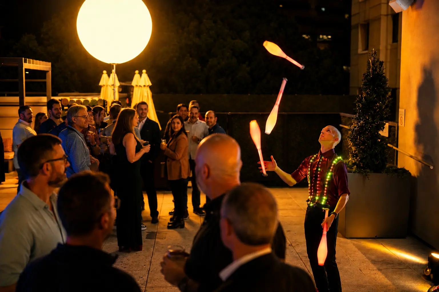 Dan juggling illuminated clubs among guests at an evening reception