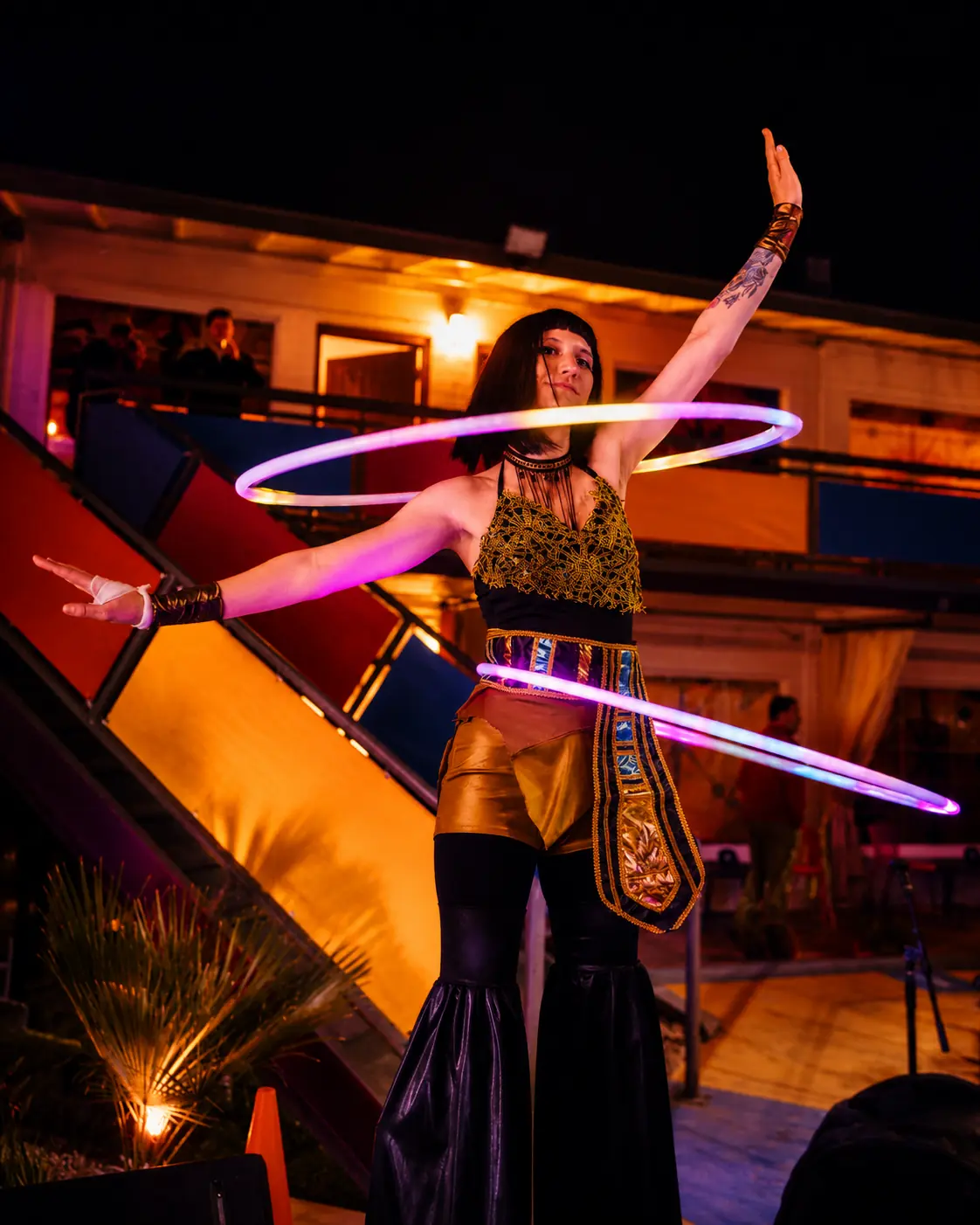 Tabitha in Egyptian-themed costuming spinning illuminated hoops while walking on stilts