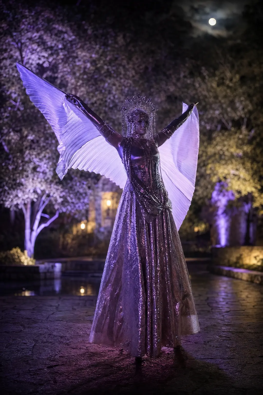 Crowned winged stilt performer in a shimmering silver gown at a moonlit Halloween event