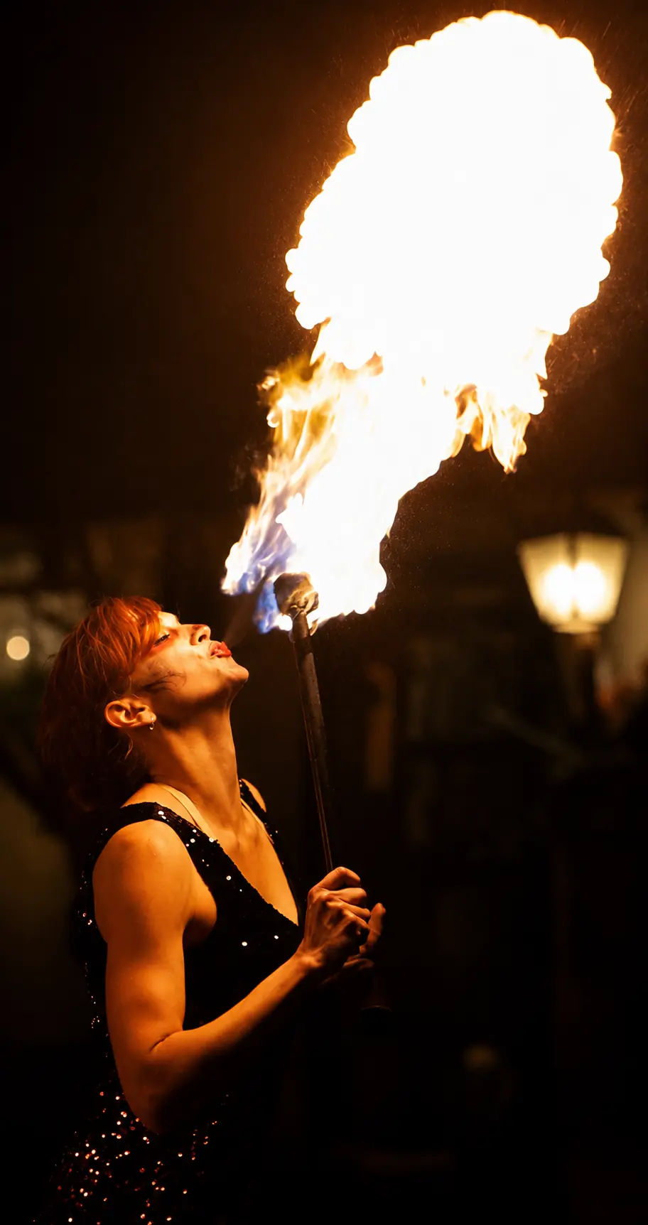 Fire performer breathing a dramatic plume of flame from a handheld torch at night