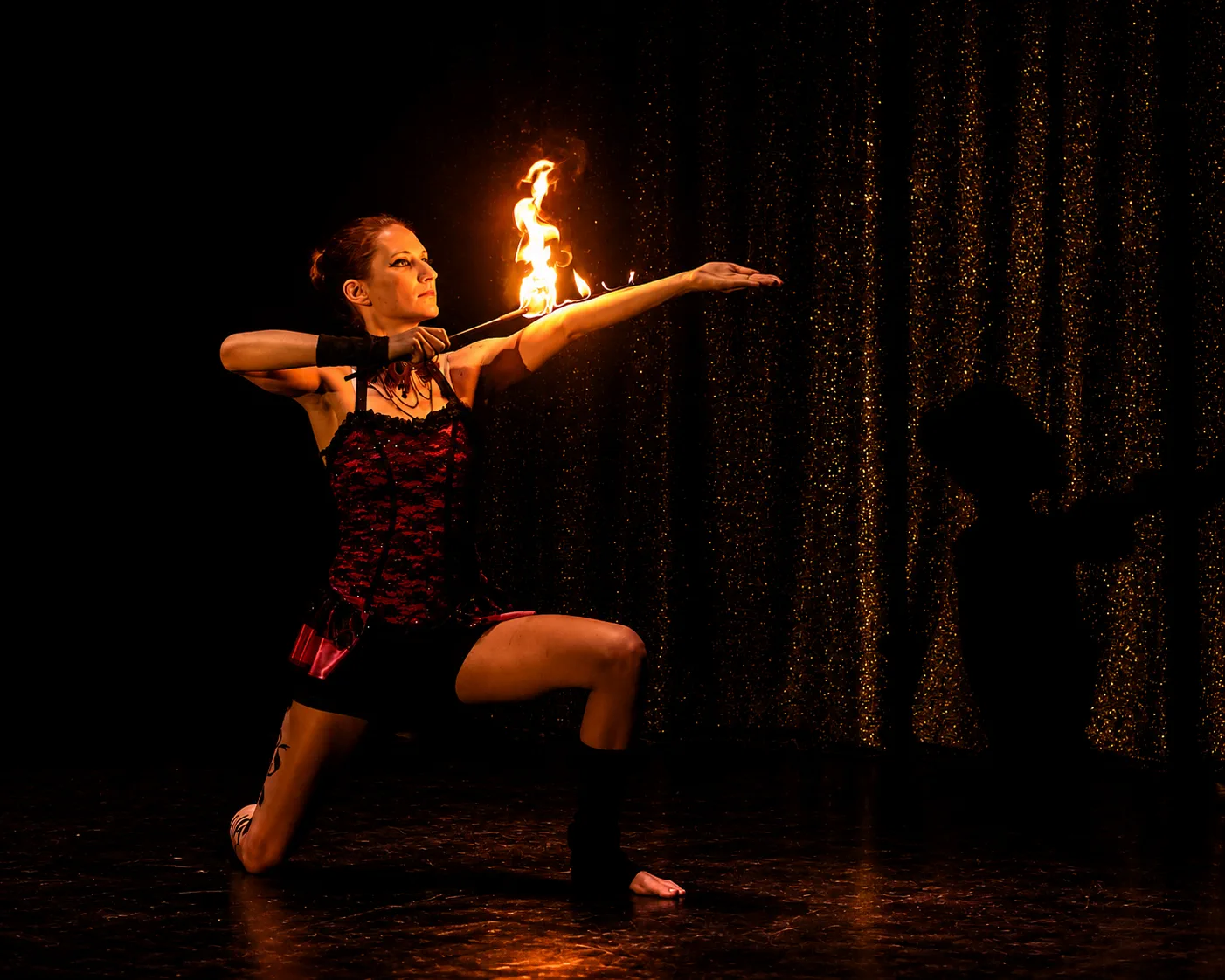 Tabitha presenting a dramatic fire torch pose on a black and gold stage