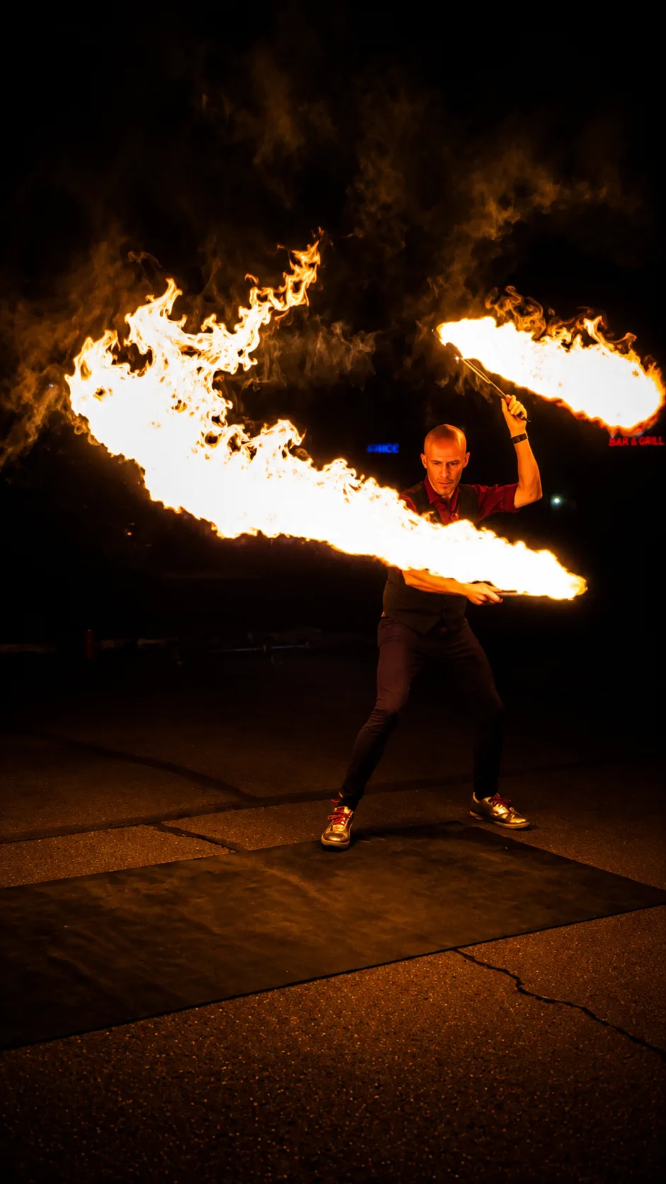 Dan creating two sweeping flame trails with large fire props during a nighttime performance
