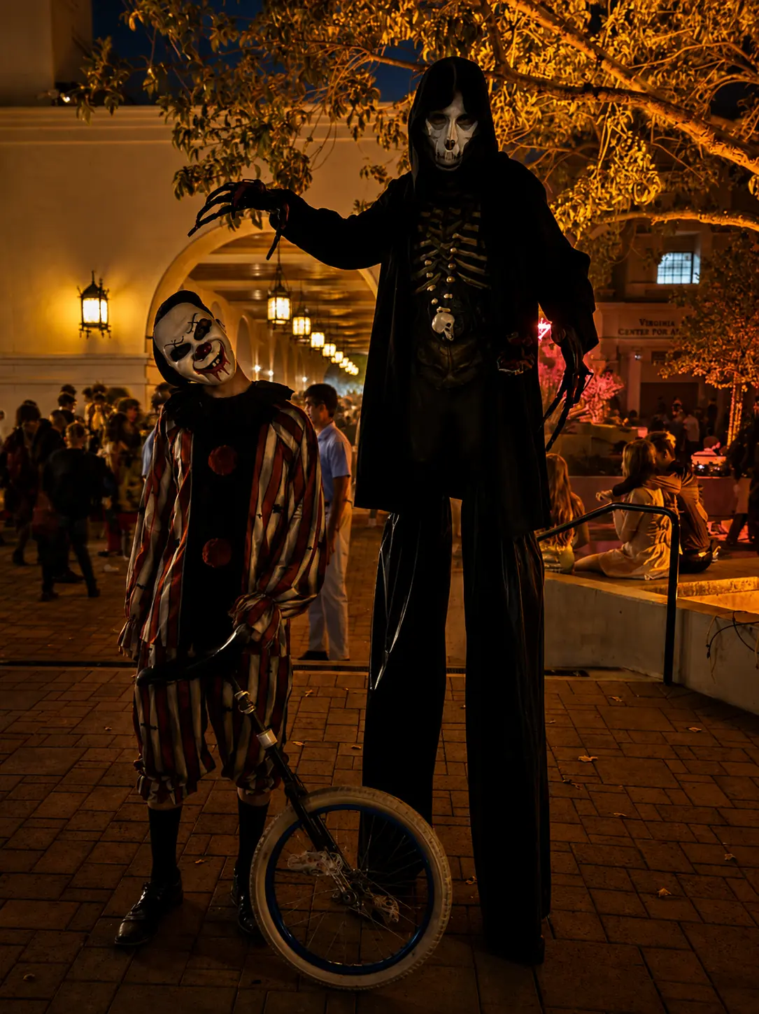 Halloween clown unicyclist posing with a towering grim-reaper stilt character