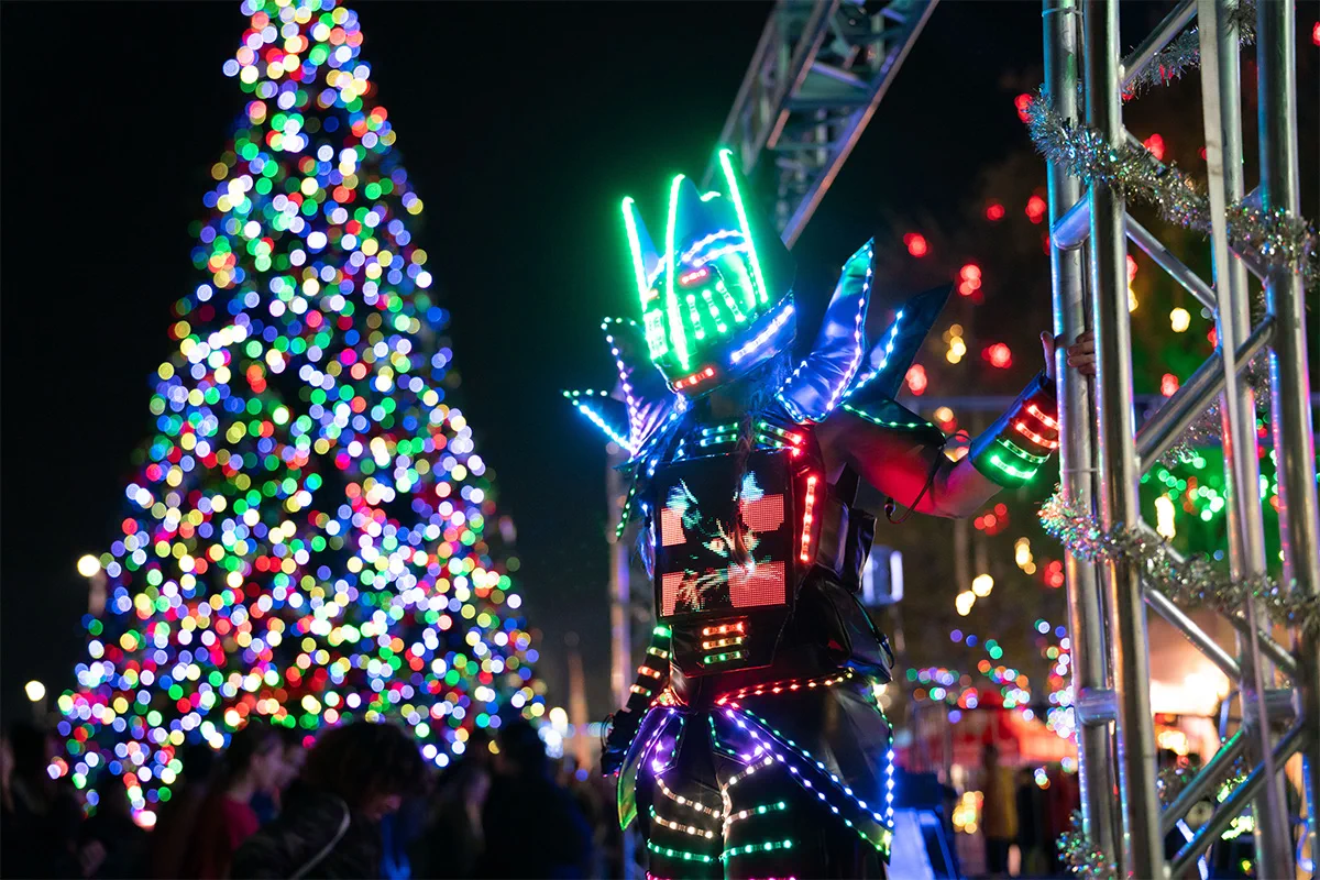 LED stilt robot appearing beside a brightly illuminated holiday tree