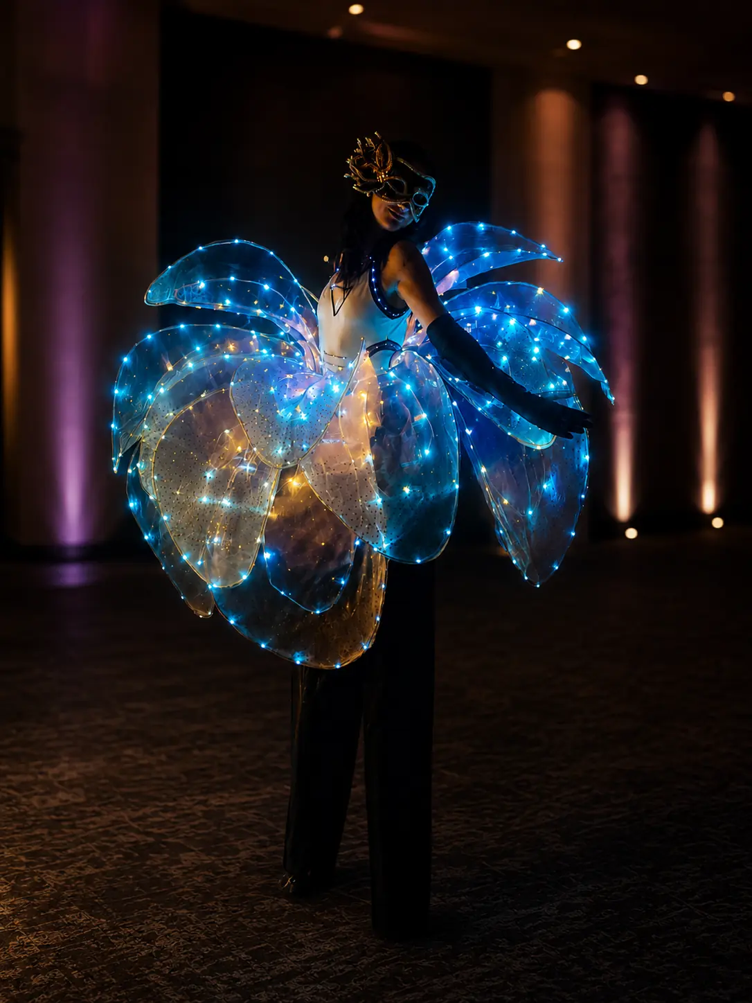 Tabitha on stilts in an illuminated blue flower-petal costume at an upscale evening event