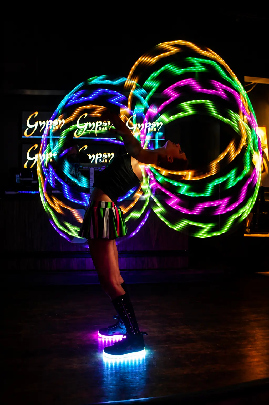 Tabitha creating multicolored light trails with multiple LED hoops during an indoor performance
