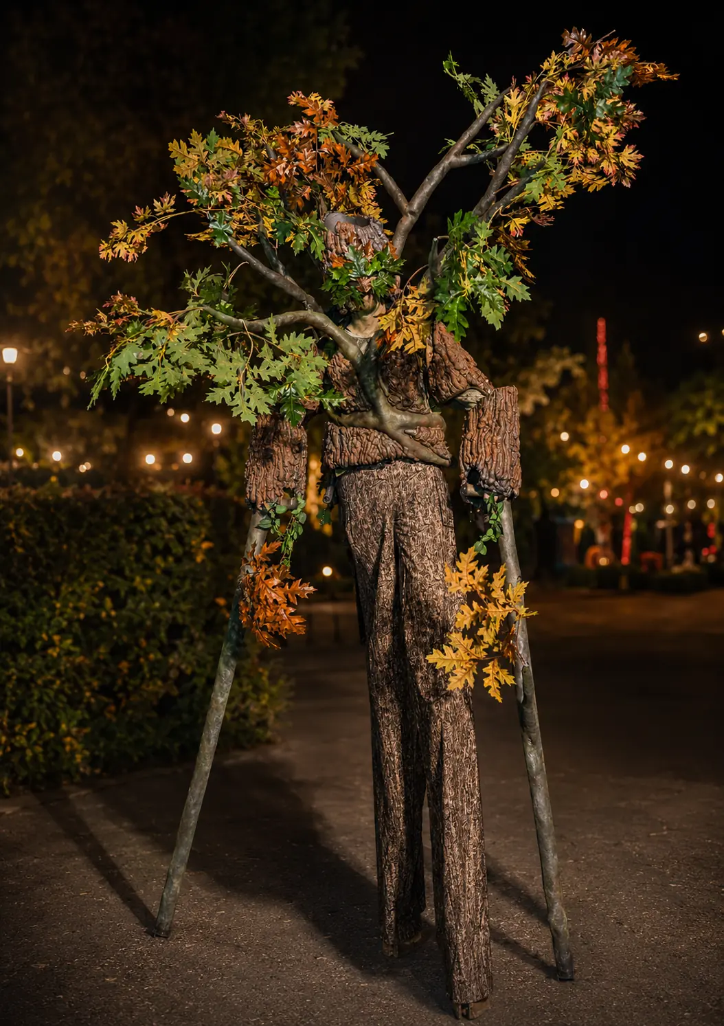 Towering tree character on stilts with branching limbs and autumn foliage at a nighttime event
