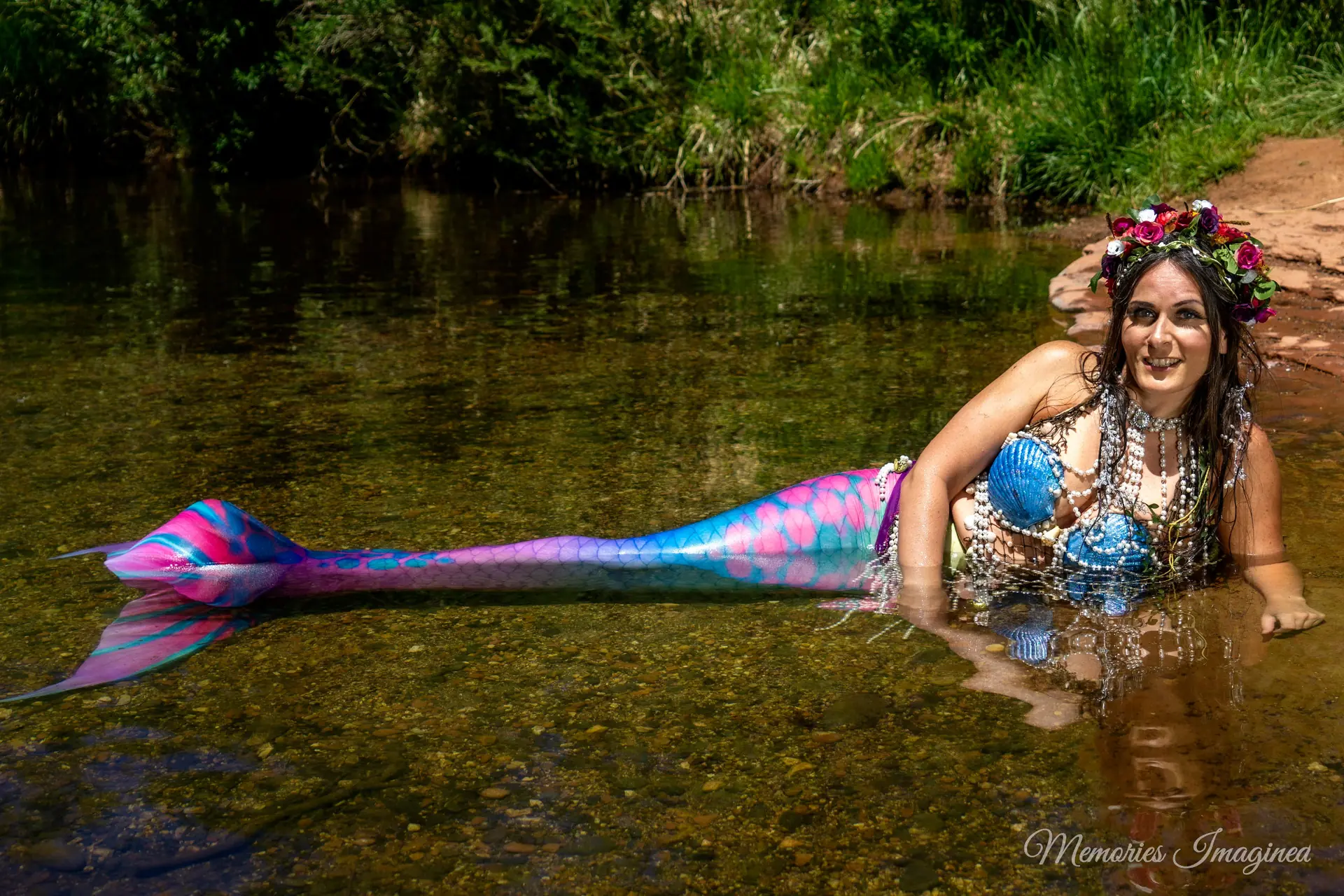 Mermaid character in a colorful costume beside a shallow creek