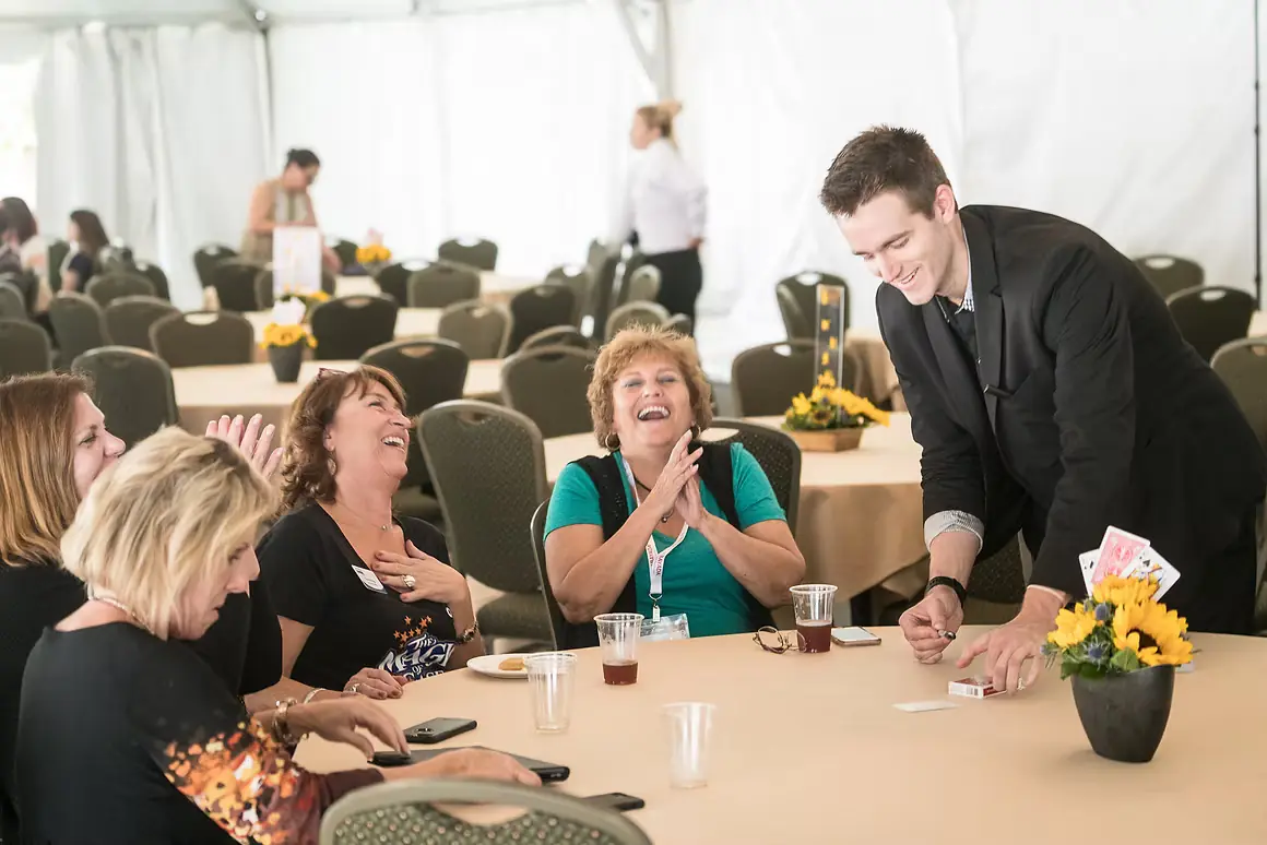 Magician Eric performing close-up card magic at a guest table during a daytime event