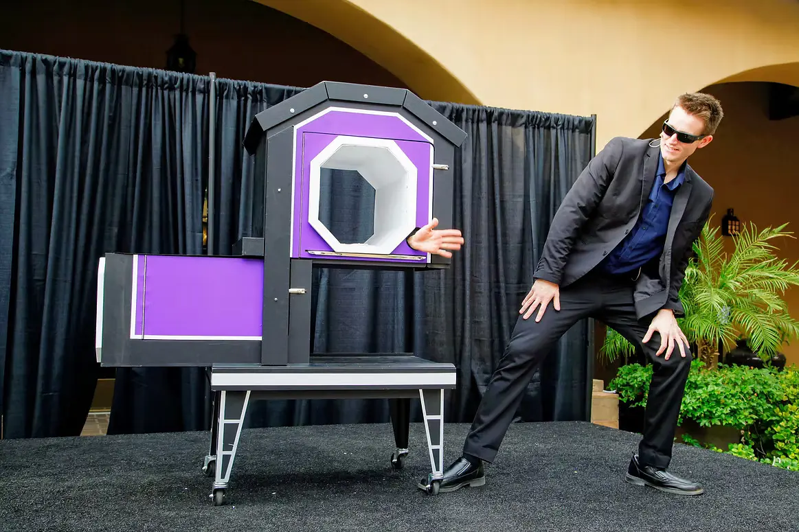 Magician presenting a stage illusion with a hand appearing through a purple cabinet