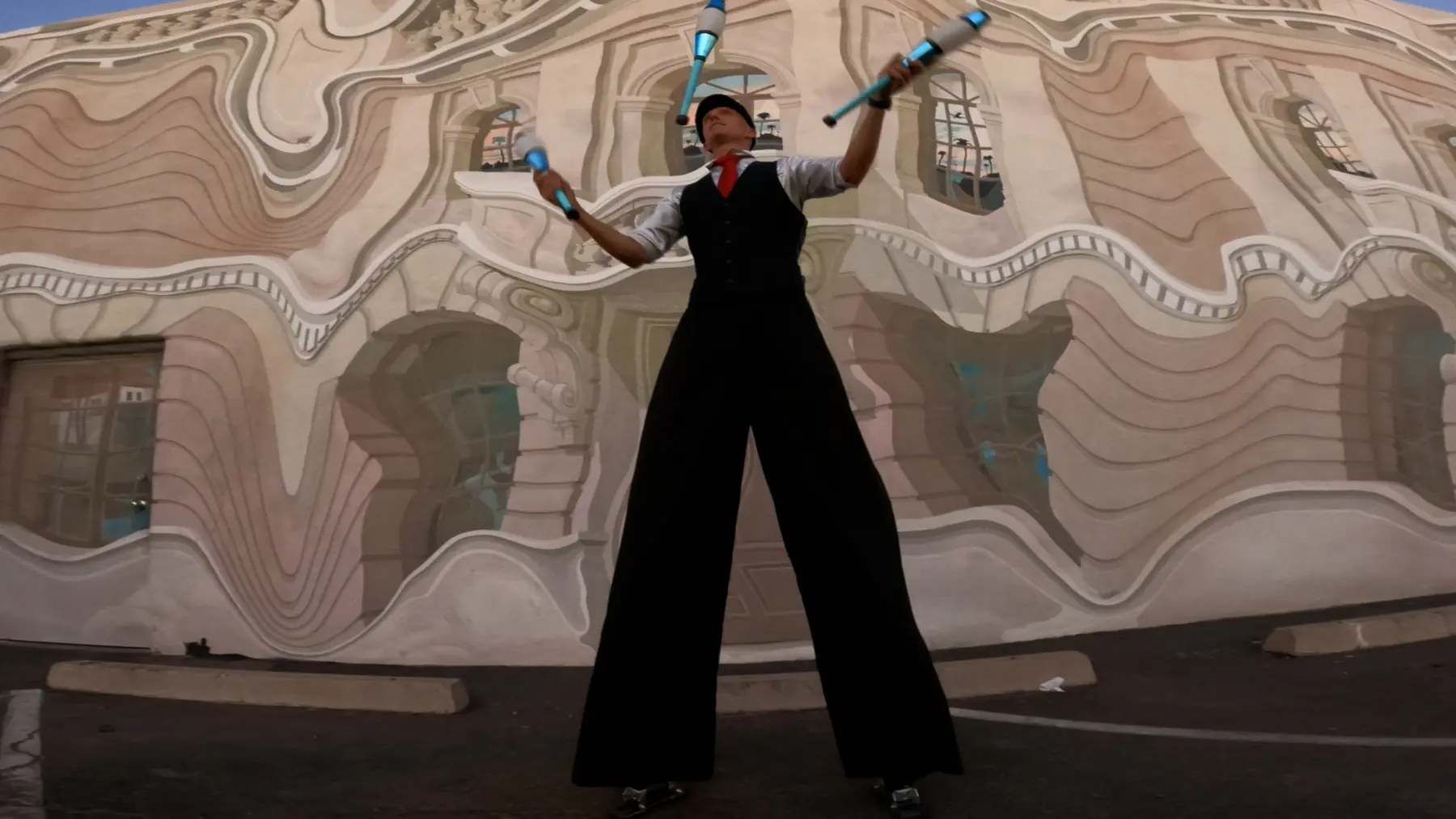 Dan juggling illuminated clubs while walking on stilts in front of an artistic mural