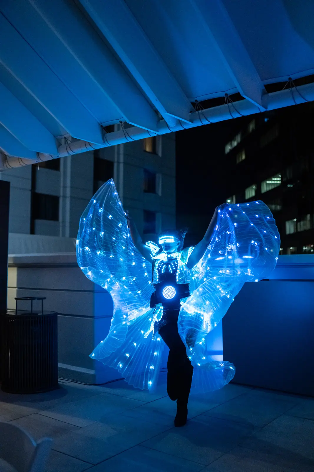 Performer presenting bright blue illuminated wings at an evening event