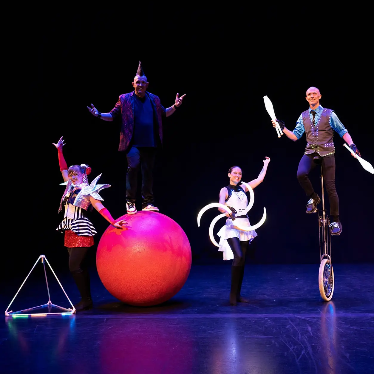 Four circus variety performers presenting walking globe, LED props, juggling clubs and unicycle onstage