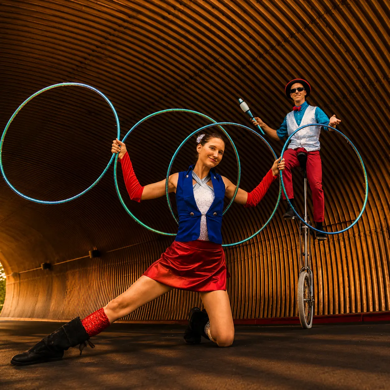 Tabitha posing with hoops while Dan balances on a giraffe unicycle