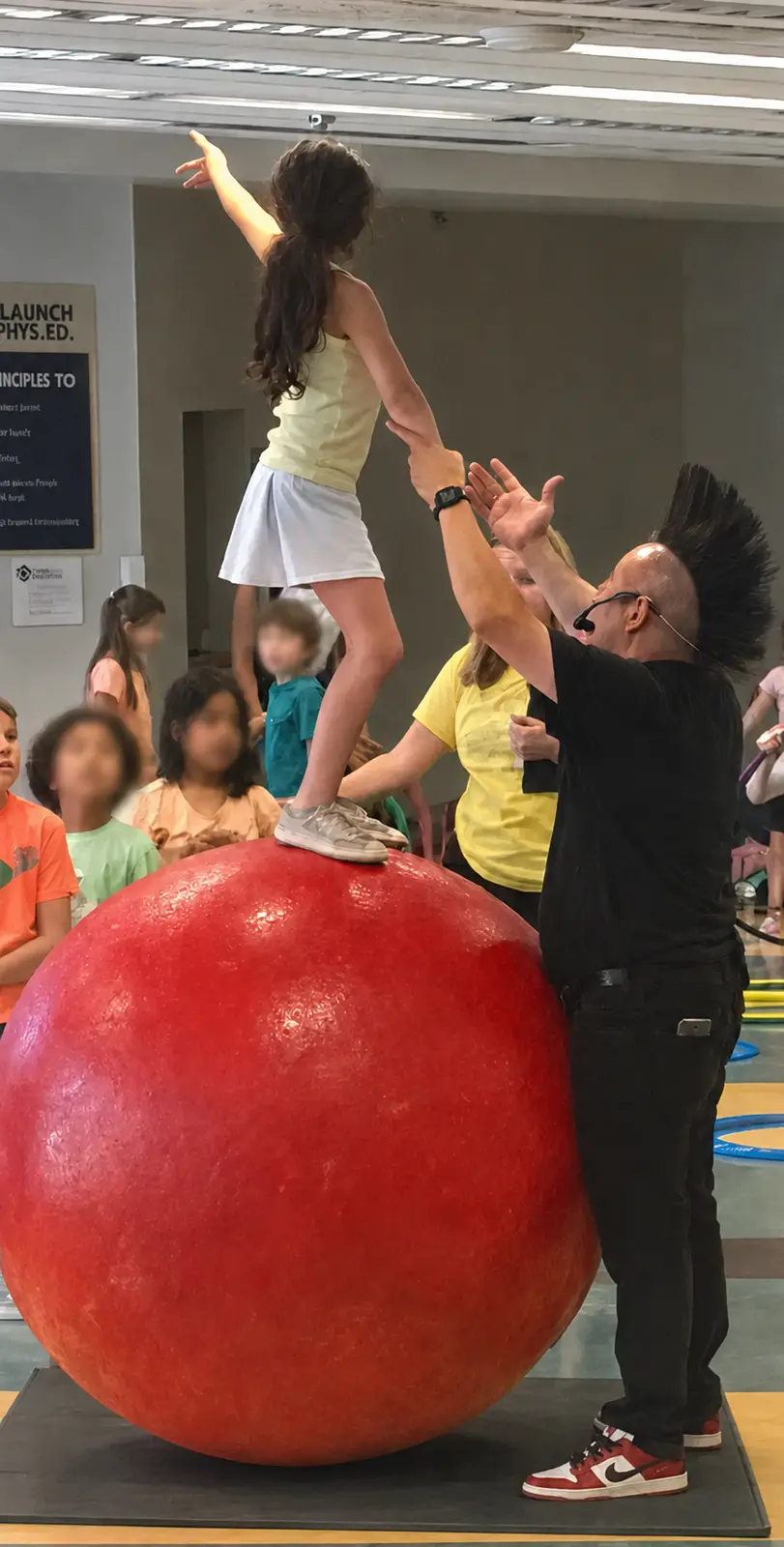 Stevie closely assisting a child standing on a stationary walking globe above a safety mat